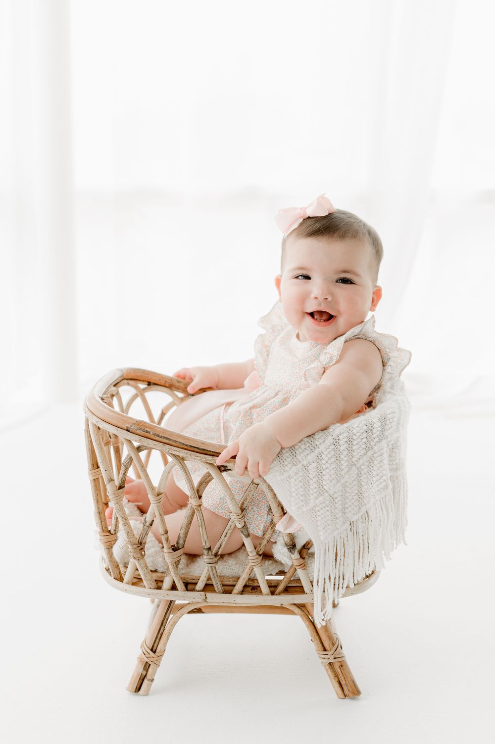 A baby sits in a rattan chair with white cushioning and macrame details in three progressive poses.