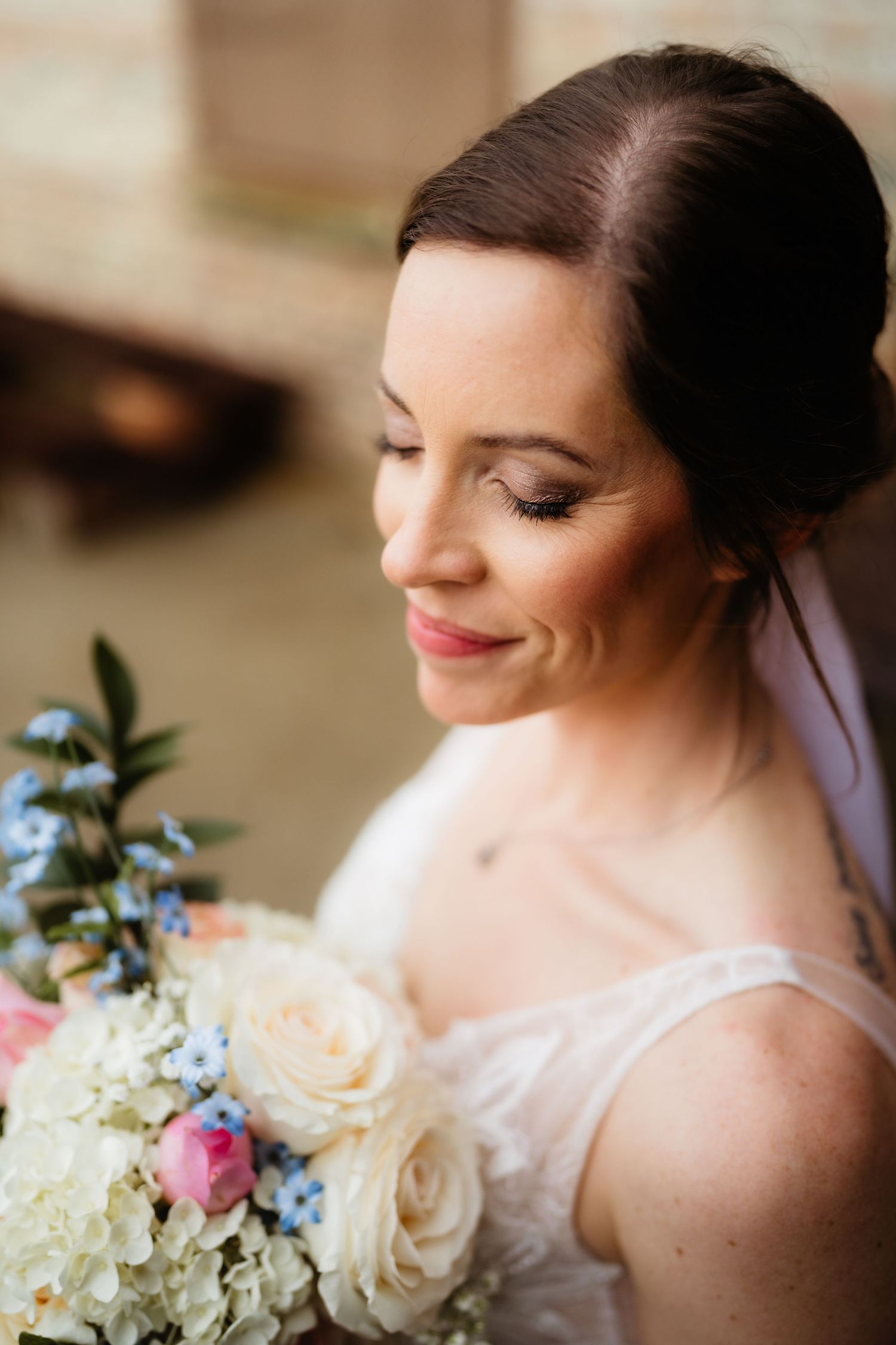Bride smiling down at bouquet of white roses, hydrangeas, and blue flowers on her wedding day.