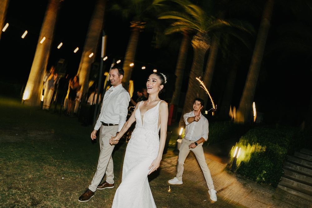 Wedding couple walking at night along a palm-lined path illuminated by outdoor lighting.