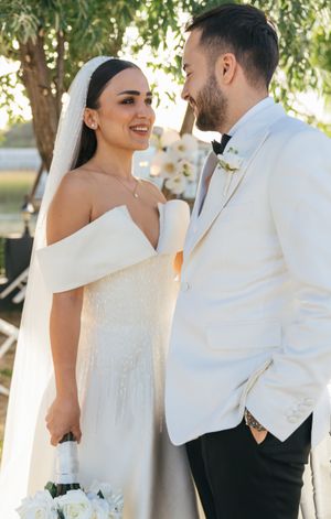Elegant couple in white attire shares intimate moment during wedding photoshoot.