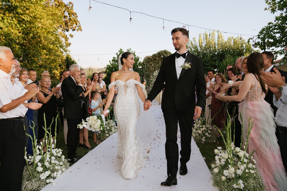 Wedding party walks along a garden path decorated with string lights and floral arrangements.