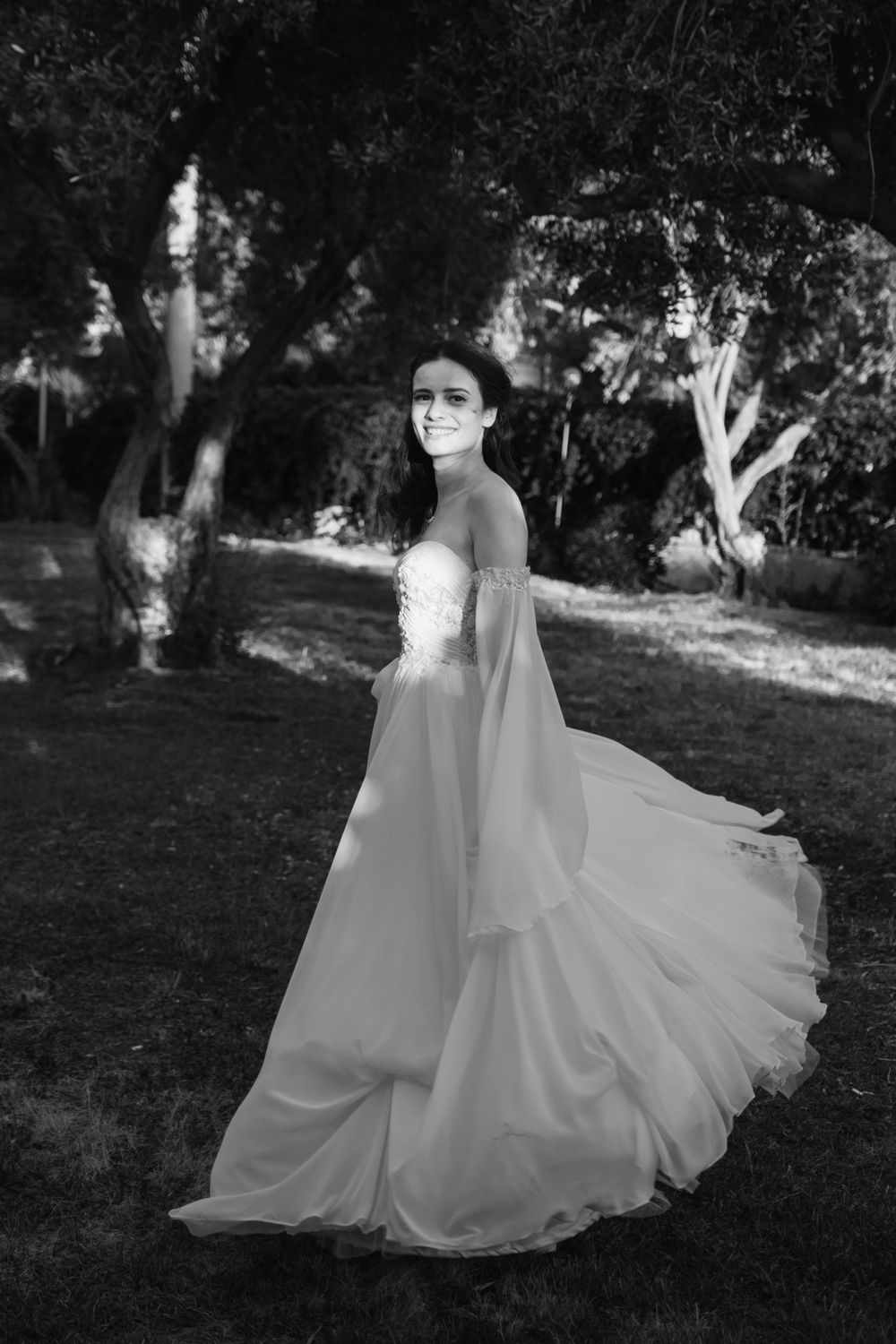 A bride in a flowing white wedding dress twirls gracefully in a garden setting creating an ethereal motion effect.