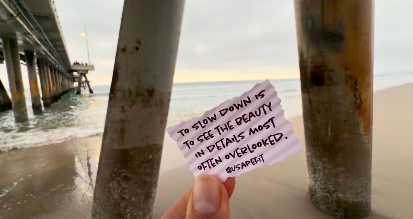 A handwritten note on pink paper is held up against a concrete pillar in an urban setting.