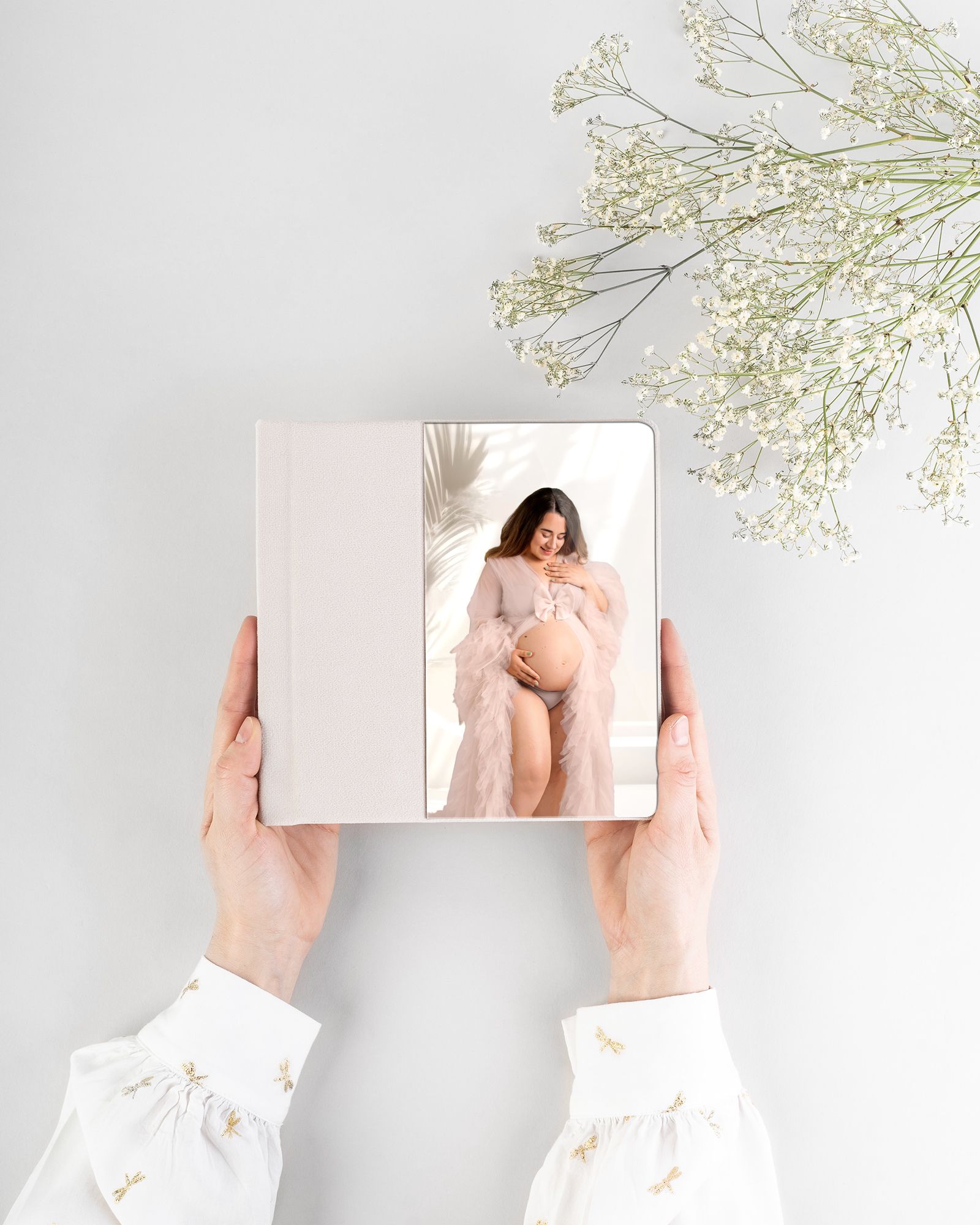 Blue leather photo album with newborn baby portrait displayed on a cream sofa beside a small matching keepsake box.