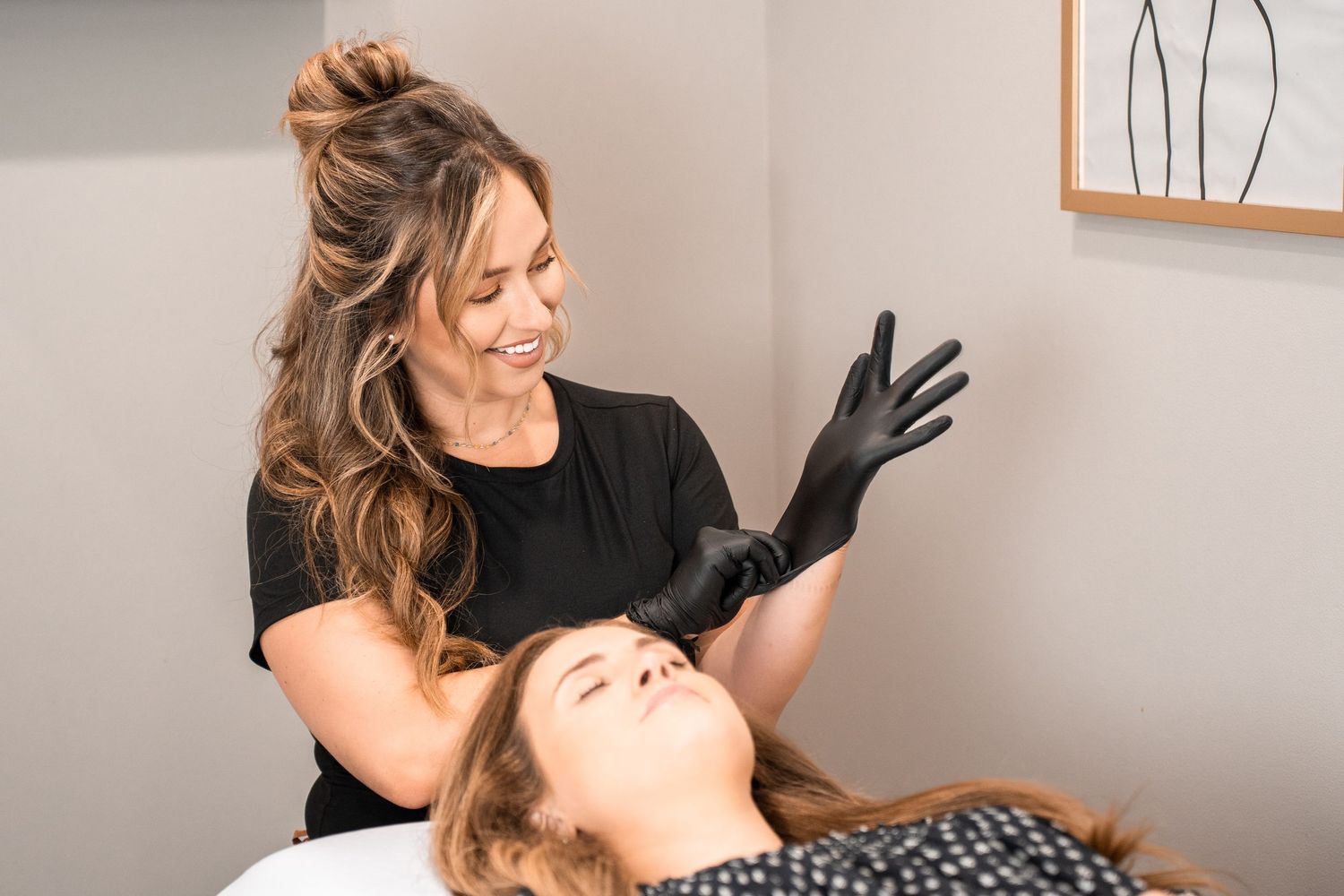 Esthetician in black gloves performing a facial treatment on a client lying down in a modern beauty salon.