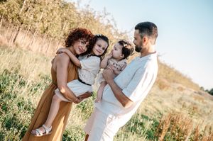 Happy family with two young daughters enjoying a sunny day outdoors in a green field.