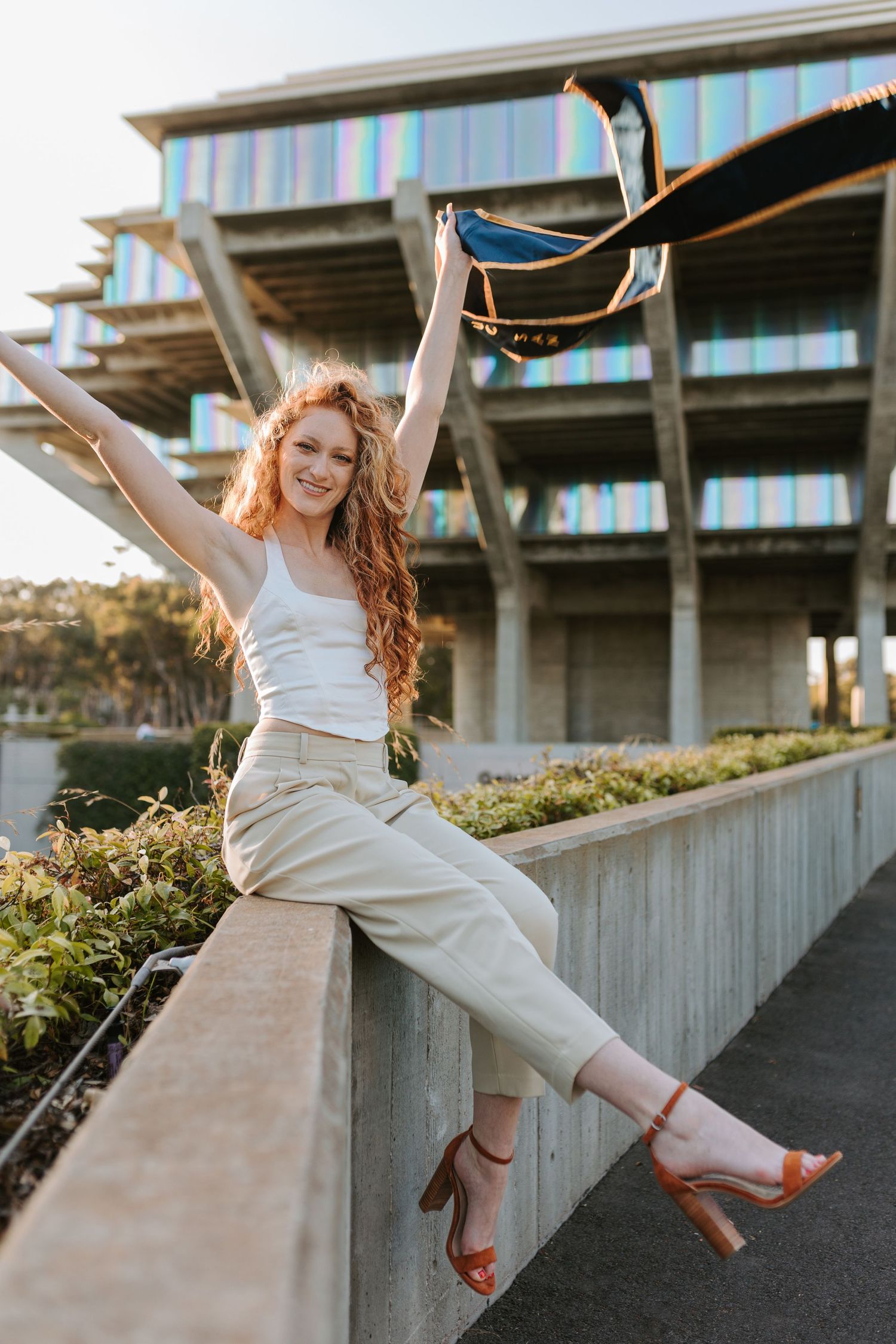 A woman with long red hair throws a blue graduation sash in the air.