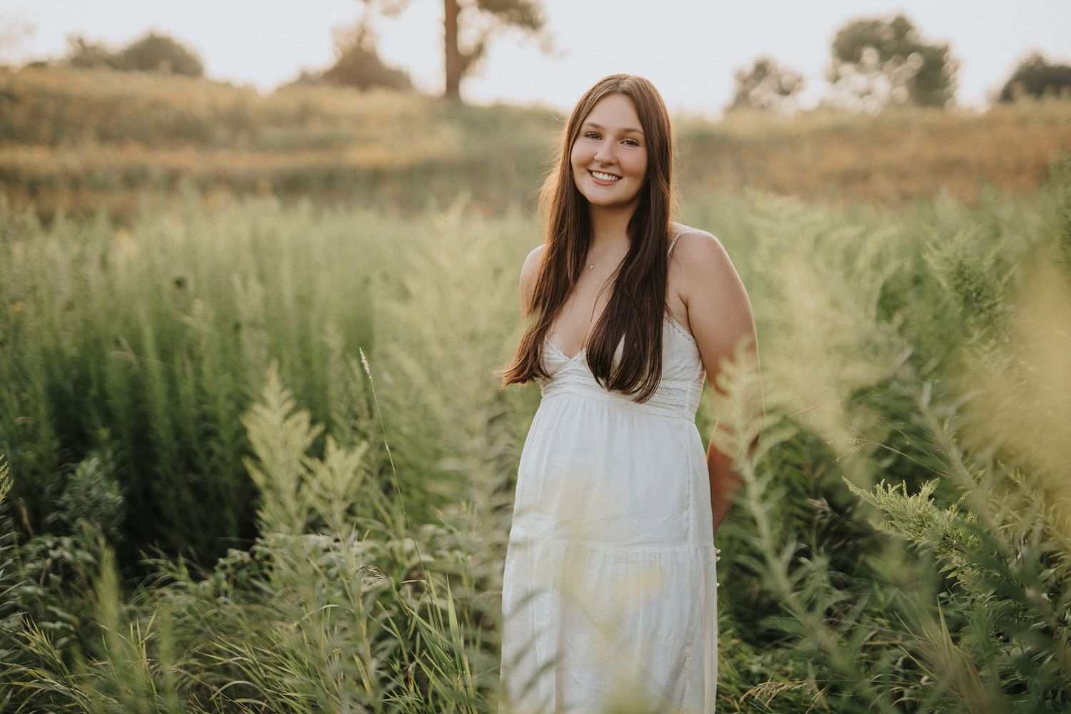 Portrait of woman with long red hair standing in tall autumn grass during golden hour.