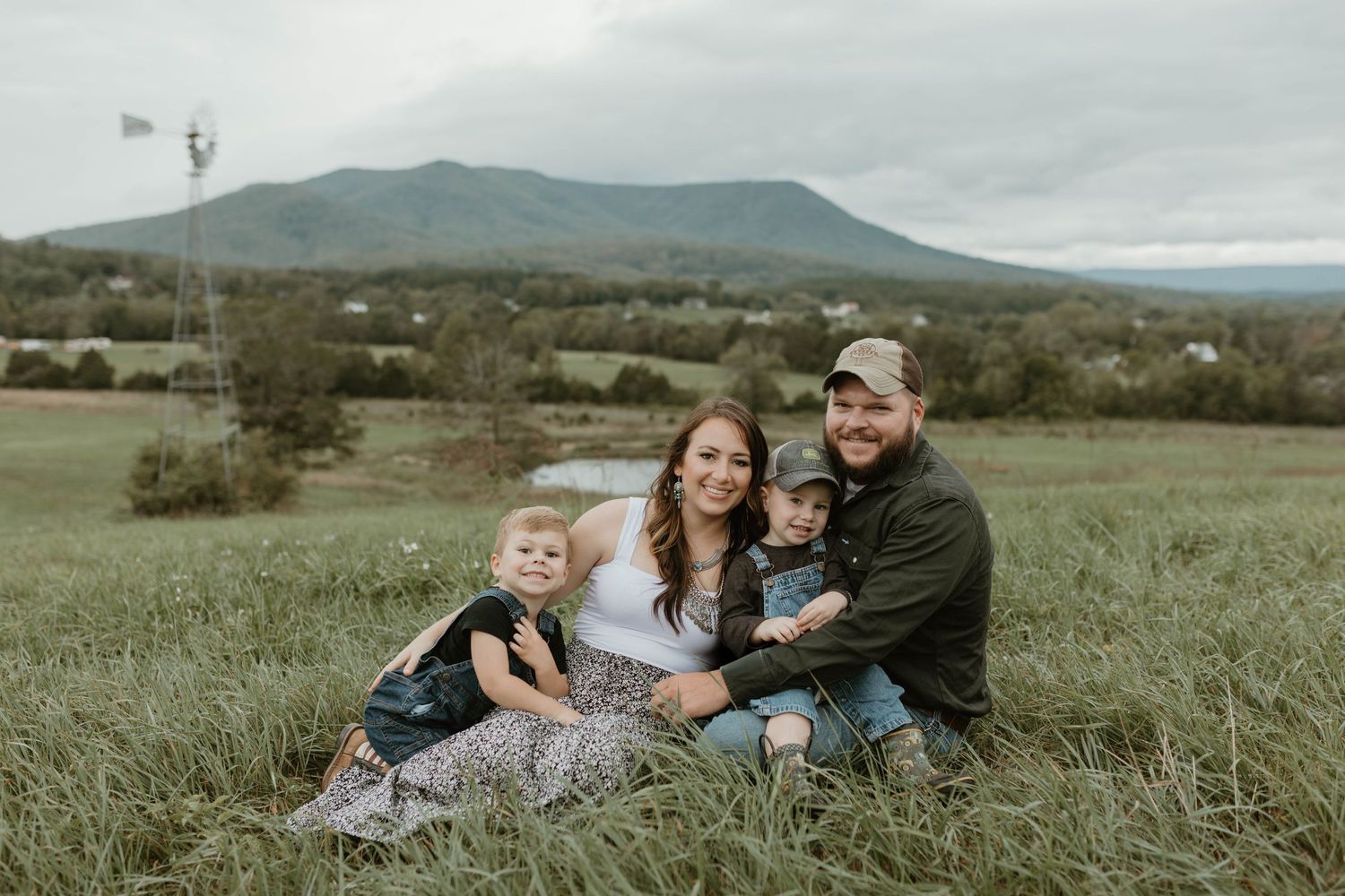 A family sitting together on grassy hillside with mountains in background during overcast day.