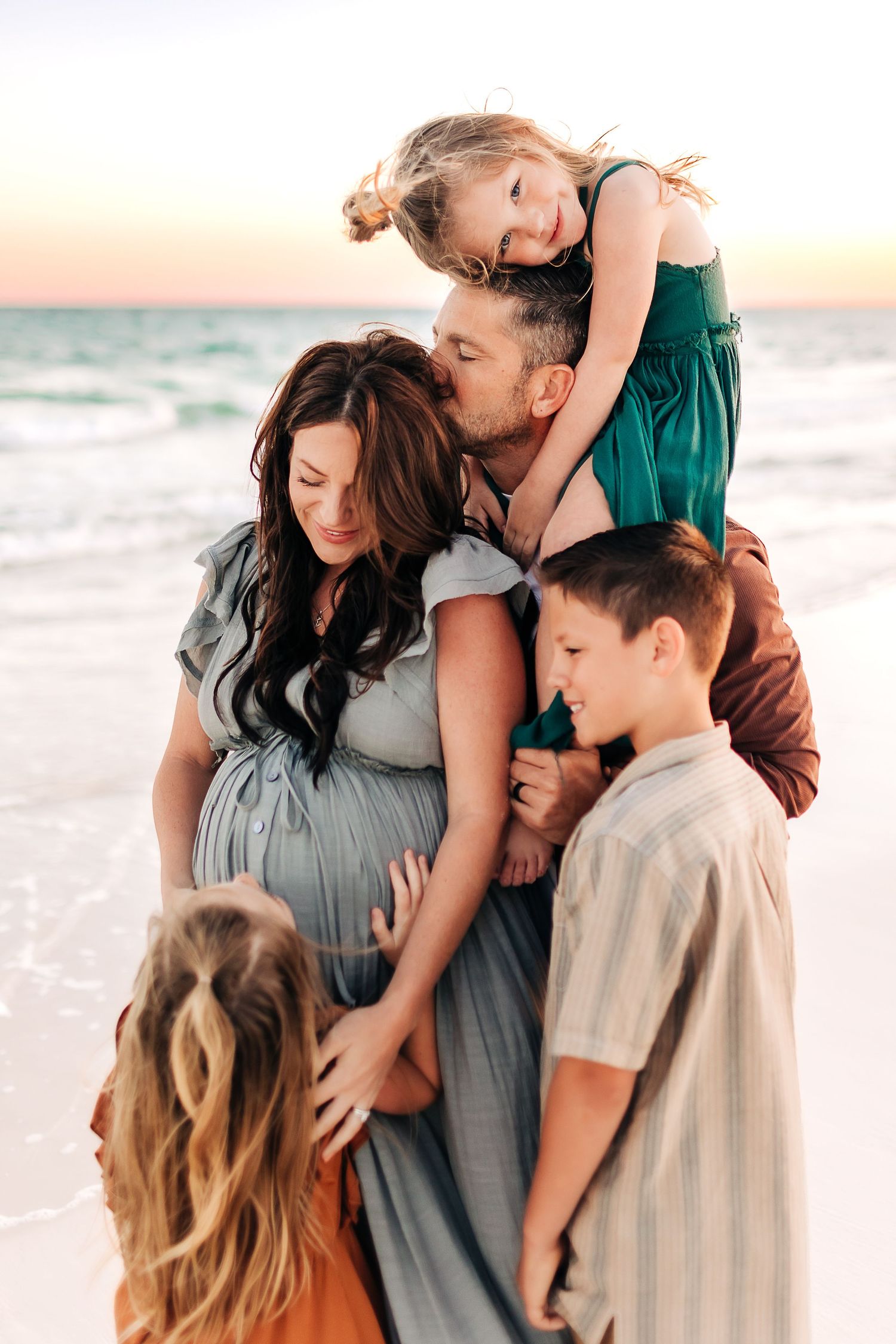 young family cuddling in navarre beach at sunset