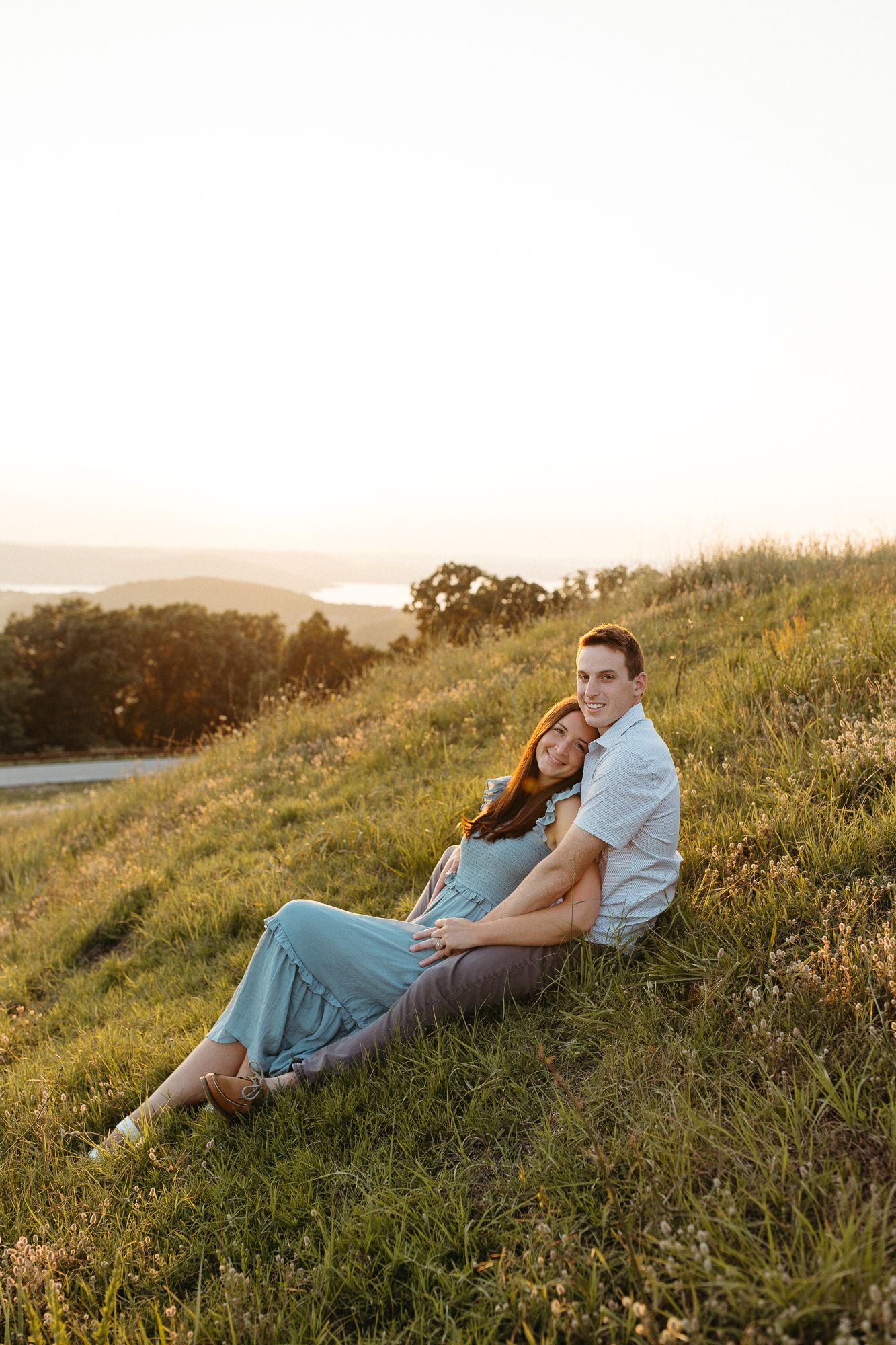 Couple sitting together on grassy hillside during golden hour sunset.