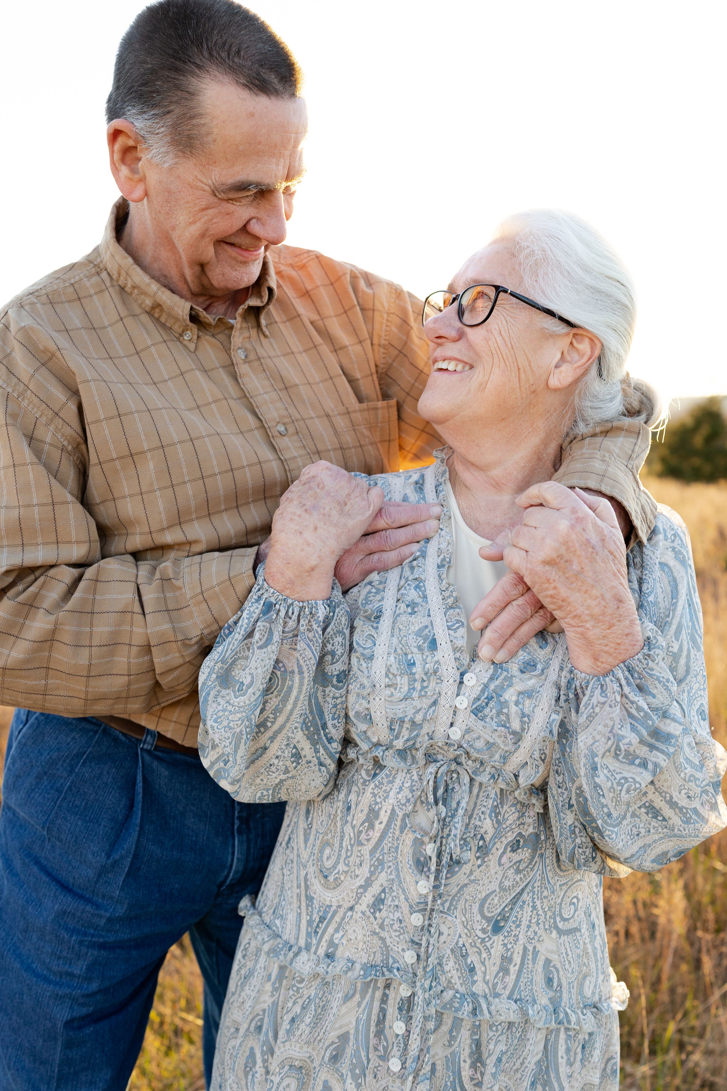 Elderly couple sharing tender moments in a field at sunset as they embrace and laugh together.