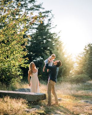 A couple stands together in a sun-drenched field with trees at sunset, creating a romantic silhouette effect.