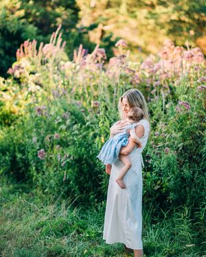 Family embraced in tender moment outdoors among blooming wildflowers during golden sunset light.