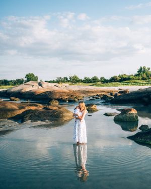 Person in a white dress standing in shallow reflective water surrounded by rock formations on a sunny day.