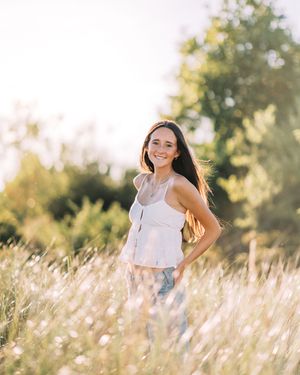 Young woman in white dress twirls happily in tall golden grass field at sunset in summer.