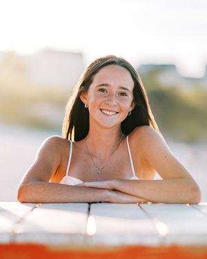Smiling woman lying down in bright natural sunlight creating an ethereal glowing portrait series against white background.