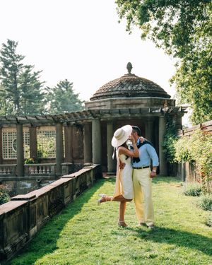 A romantic couple sharing an intimate moment on a stone terrace surrounded by greenery and classical architecture details.