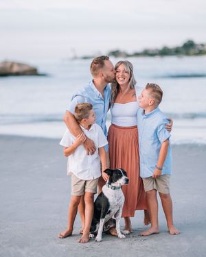 A loving family shares a joyful moment together on the beach at sunset with their black and white dog.