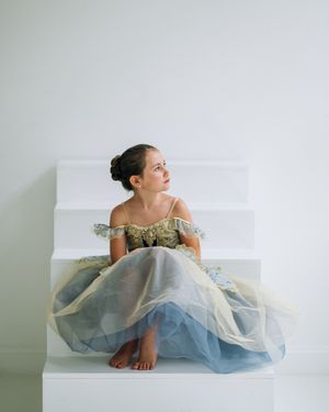 Dancer wearing a flowing blue tulle gown poses gracefully on a white backdrop in a minimalist modern setting.