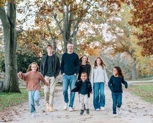 Happy family of seven walking together on a scenic autumn path surrounded by colorful fall foliage.