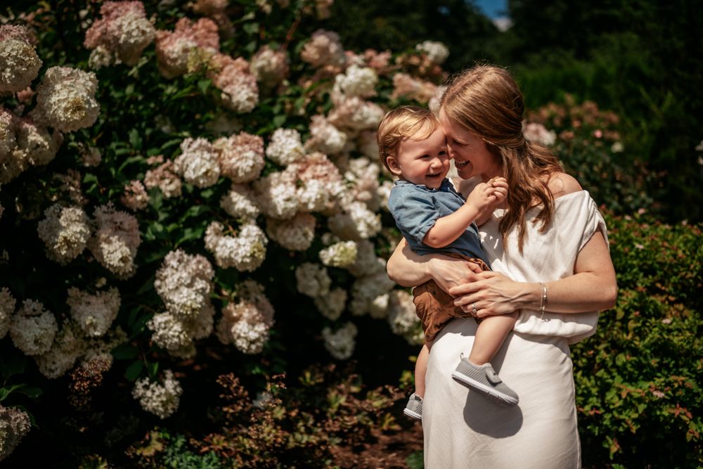 Sweet family moment captured against a backdrop of blooming pink roses in a garden setting.