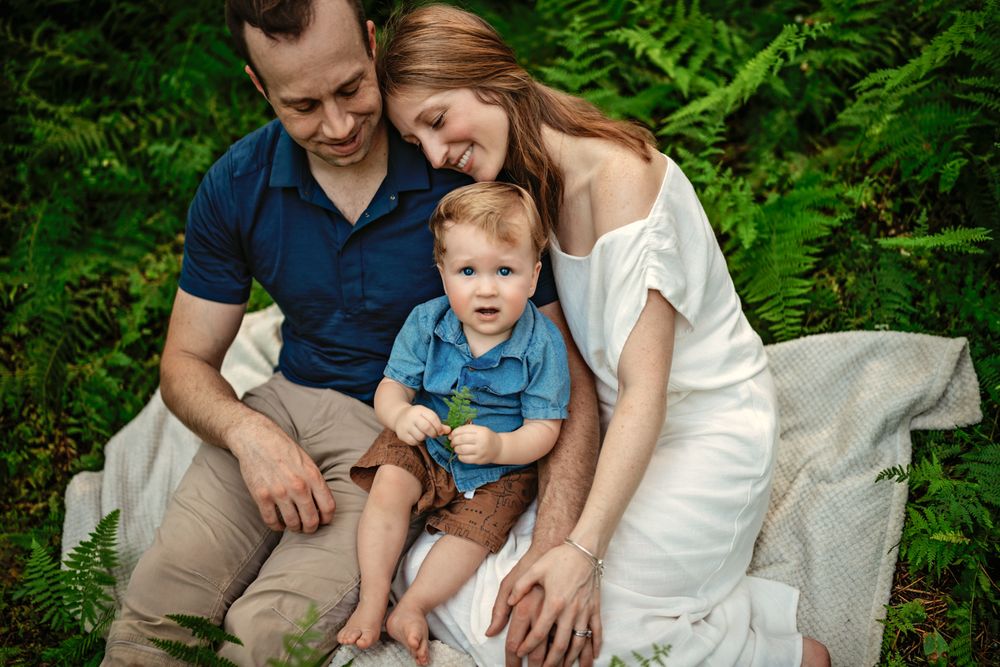 Family enjoying a tender moment together while sitting on a blanket in a lush green forest setting.