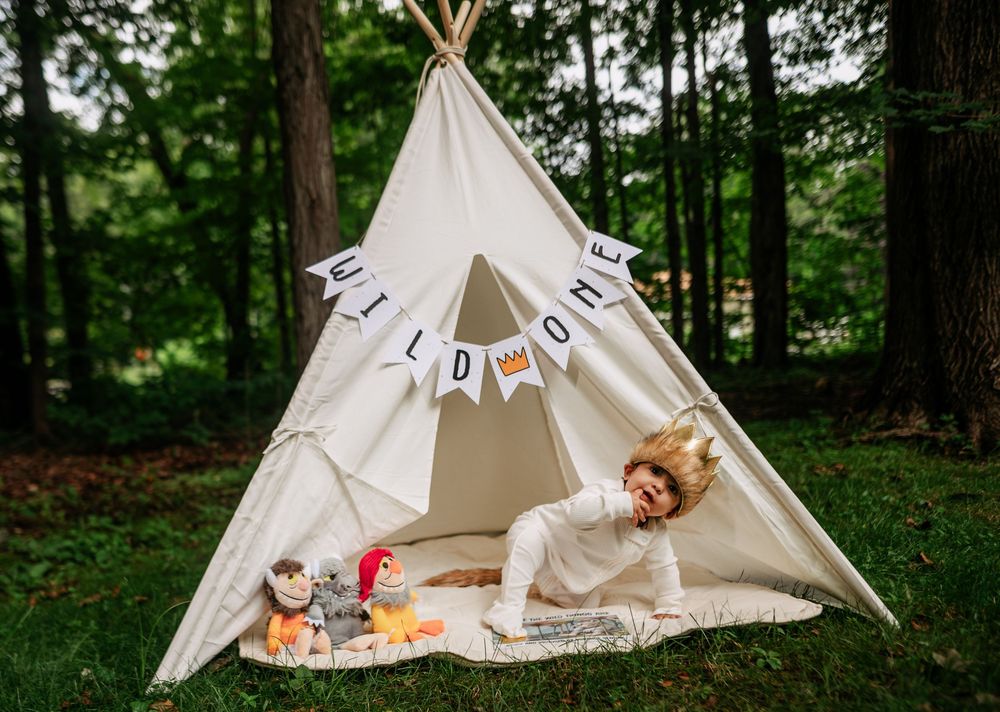 A series of white teepee tents arranged in a lush green forest setting creates a whimsical outdoor scene.