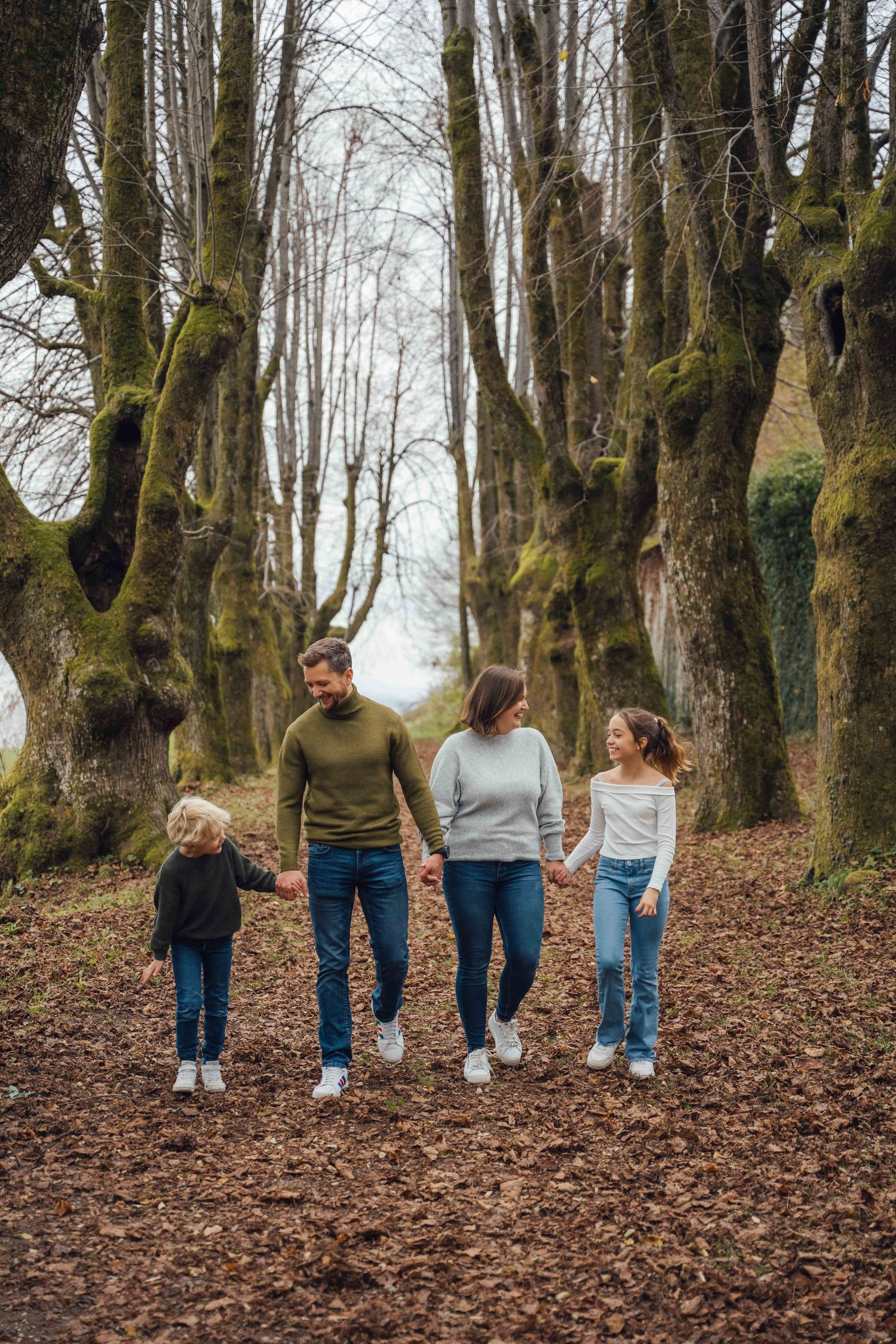 Family walking together through autumn forest path holding hands.