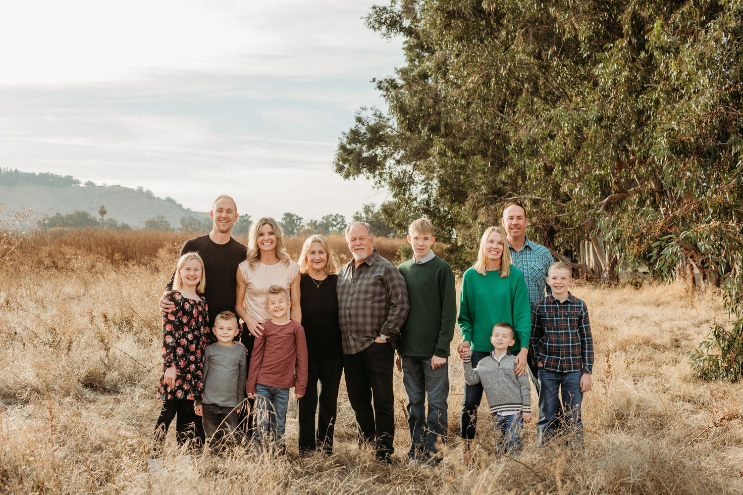 Family group portrait taken outdoors in golden field with mountains in background.