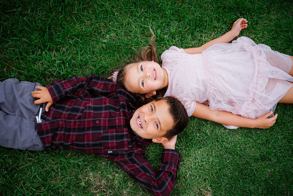 Children lying on green grass during outdoor family photoshoot.