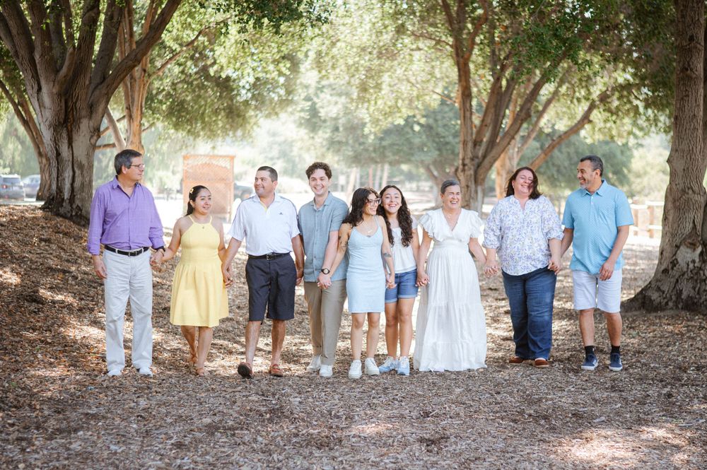 Family group poses under shaded tree canopy in casual outdoor setting.
