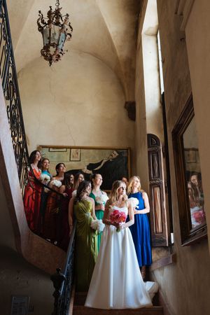 Mariée et ses amies dans l'escalier d'honneur d'un château, moment solennel capté dans un lieu chargé d’histoire.