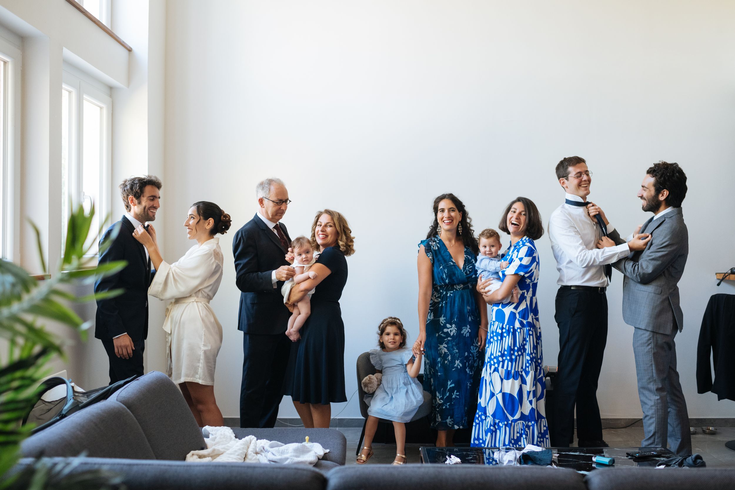 Famille et proches réunis dans une pièce lumineuse avant la cérémonie, ambiance chaleureuse et spontanée.