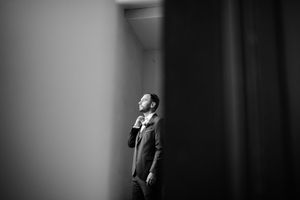 Portrait en noir et blanc d’un futur marié éclairé par une lumière douce d'une fenêtre dans une chambre.