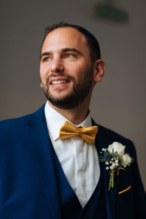 Portrait du marié en costume bleu et nœud papillon jaune, regard souriant et élégant.