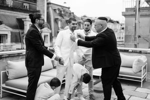 Scène en noir et blanc du marié entouré de ses proches pendant les préparatifs, ambiance vivante et chaleureuse.