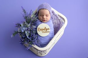 Newborn baby Rosalyn Victoria swaddled in purple wrap with lavender flowers in a white wicker basket.