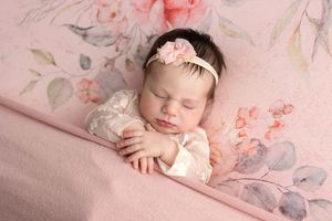 Newborn baby girl sleeping peacefully on pink floral blanket wearing lace outfit and pink flower headband.