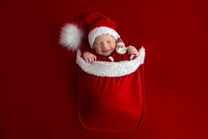 Newborn baby sleeping in a red Santa sack wearing a Santa hat on a red background.