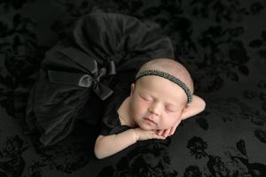 Newborn baby girl sleeping peacefully in black tutu and headband on dark floral background.