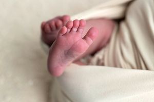 Close-up of tiny newborn baby feet wrapped in soft cream blanket, perfect newborn photography detail shot.