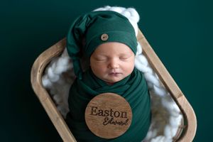 Newborn baby named Easton Edward swaddled in green wrap and hat, sleeping peacefully in wooden bowl prop.