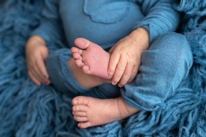 Close-up of newborn baby feet and hands in blue outfit on soft blue fluffy blanket.