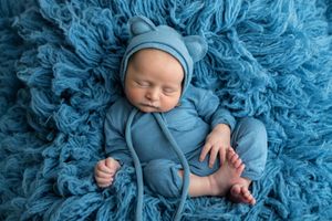 Sleeping newborn baby in blue bear outfit and hat on fluffy blue textured blanket.