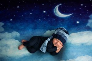 Newborn baby sleeping peacefully on clouds under a crescent moon in a dreamy night sky photo.