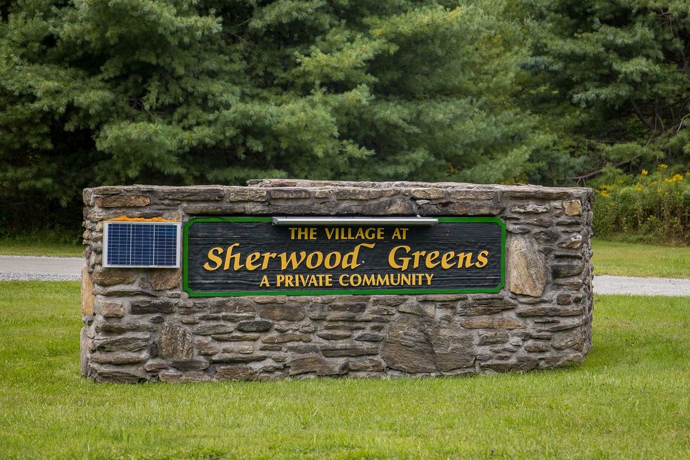 Stone entrance sign for The Village at Sherwood Greens private community surrounded by green trees.