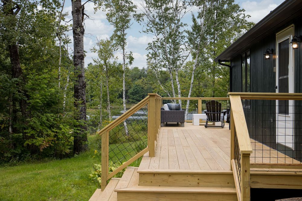 Wooden deck with cable railing overlooking lush green trees and a serene lake view.