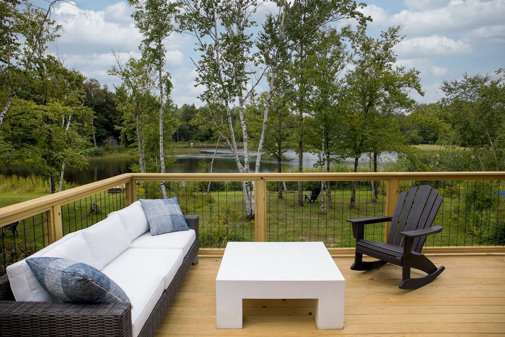 Outdoor deck furniture with white sofa and Adirondack chair overlooking a tranquil lakeside setting.