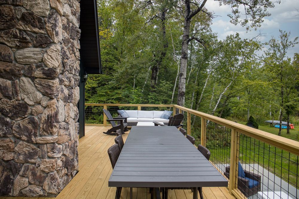 Gray outdoor dining set on cedar deck beside rustic stone wall surrounded by lush forest.